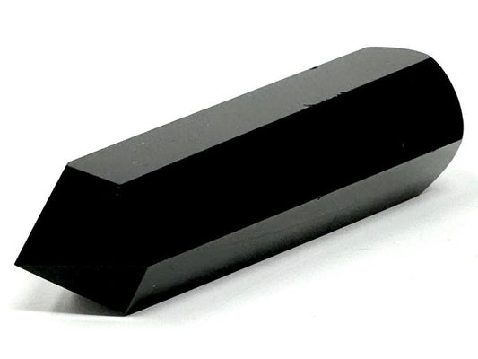 Black Obsidian Crystal Wand laying horizontally on a surface, and showing one sharp point and multiple polished faces made of Black Obsidian Stone/ Volcanic Glass